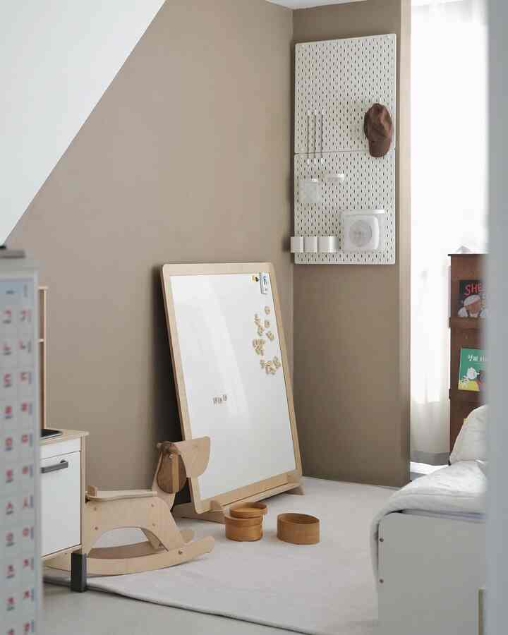 ブラウンの壁と白いカーペット、木製のおもちゃとホワイトマグネットボードが配置された子供部屋のインテリア