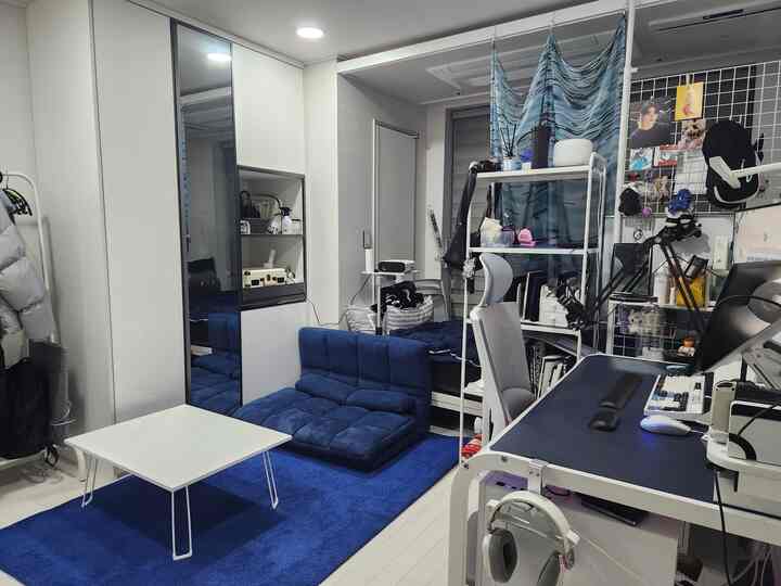 白い壁と青いソファベッドが配置された、一人暮らし向けの小さなモダンなホームオフィス空間