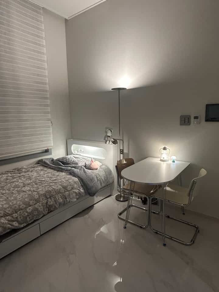 Gray and white toned 6-pyeong studio apartment featuring single bed, small dining table, and IKEA lighting with cozy ambiance