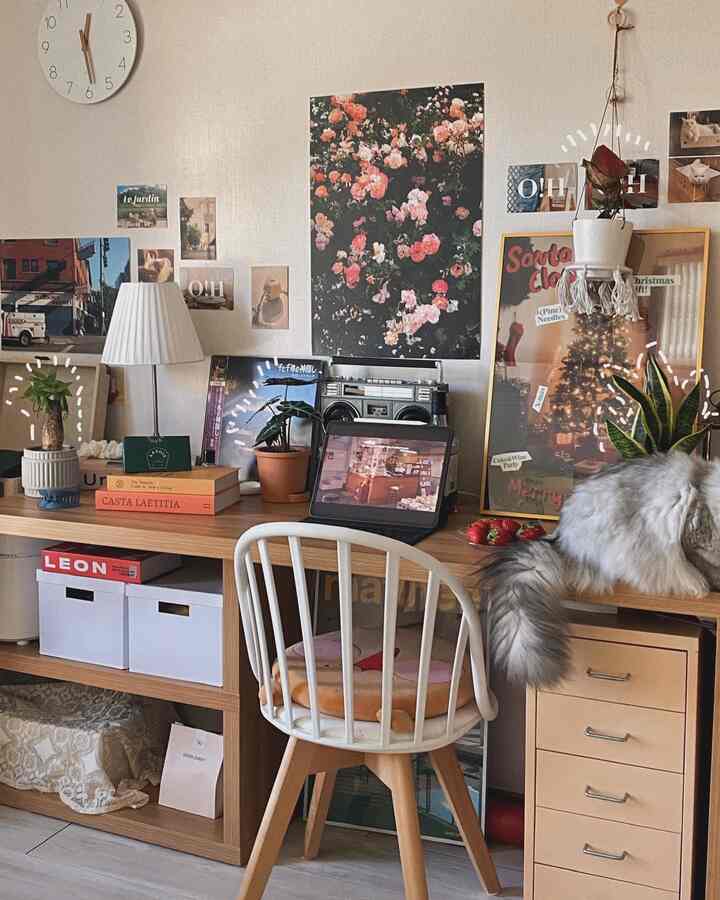 Natural wood tone and white home office featuring a cozy desk with a relaxed cat, assorted plants, and decorative posters creating a warm ambiance