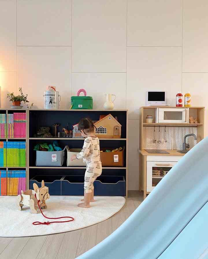 明るくナチュラルな色調の子供部屋、玩具収納とままごとキッチンが配置され、子供がラグの上で遊ぶ温かみのある空間