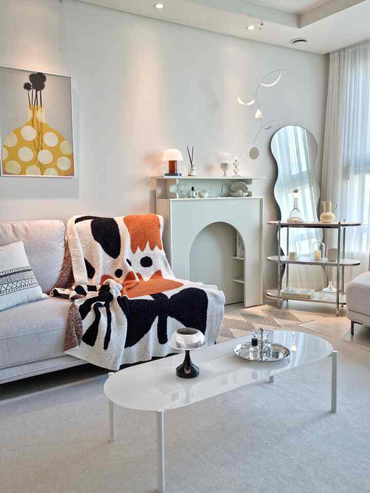White and minimal toned living room featuring fabric sofa, oval white coffee table, large poster, and minimalist shelf creating cozy atmosphere