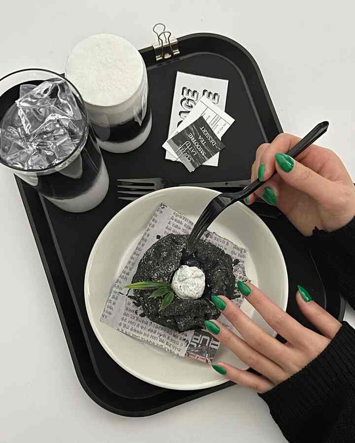 Monotone home cafe setup featuring a black tray with various drinks and a black bread on newspaper-like paper, styled with chic objet decor