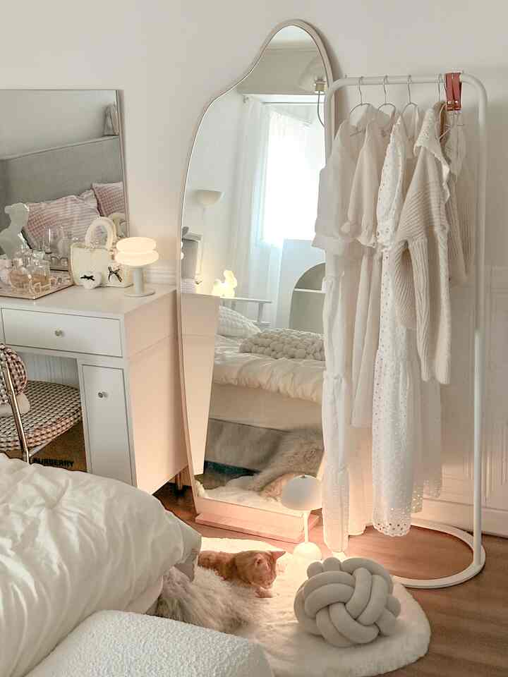 ホワイトとナチュラルカラーの寝室、変形の全身鏡と白いハンガーに服がかかる、温かみのある雰囲気のあるインテリア
