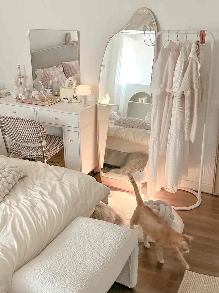 Natural and white toned bedroom featuring an irregular full-length mirror, white clothes rack, cozy lighting, and a cat walking inside