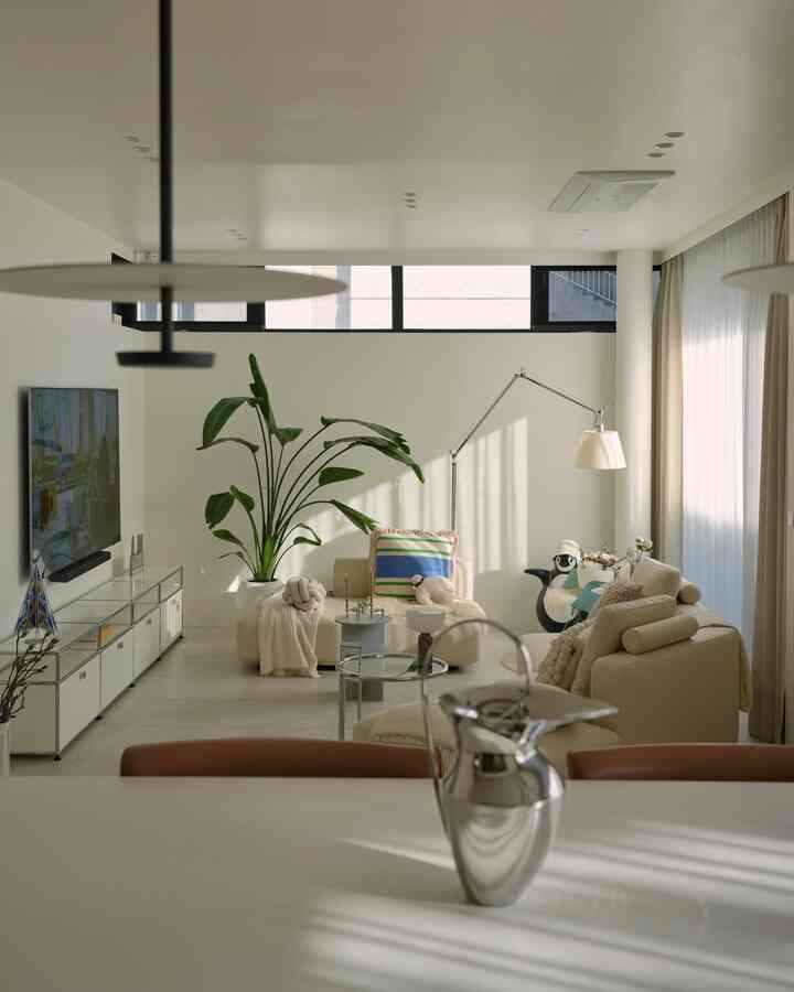 Modern living room in beige and ivory tones featuring modular sofas, floor lamp, and large indoor plant with a bright and cozy atmosphere