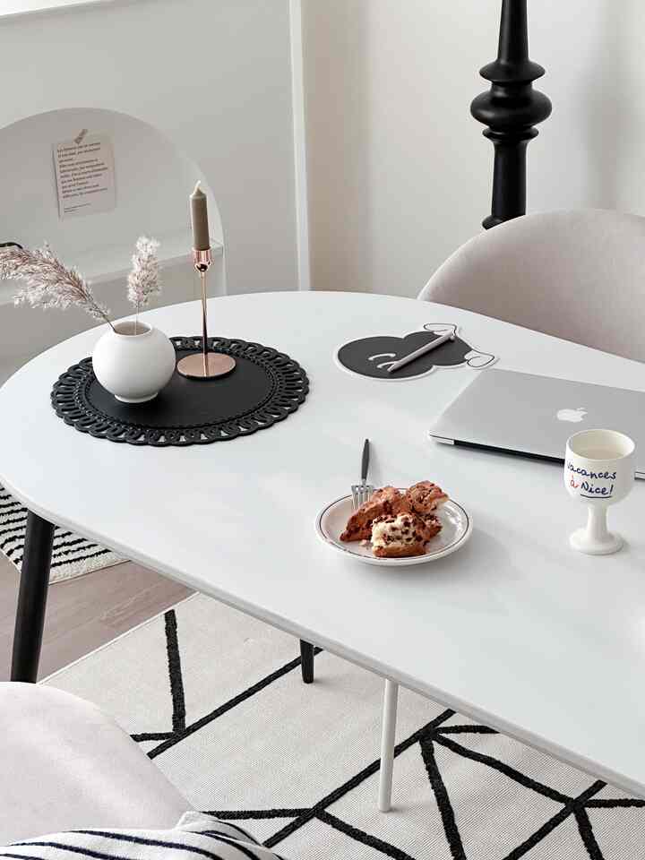 Bright white-toned modern Nordic dining room featuring a dining table with a laptop, candle holder, vase, and food creating a clean atmosphere