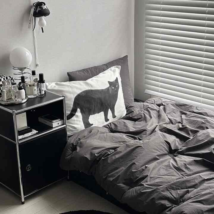 モノトーンのグレーとブラックの寝室、猫の絵柄の枕と黒いサイドテーブルが置かれたモダンで落ち着いた雰囲気のあるインテリア