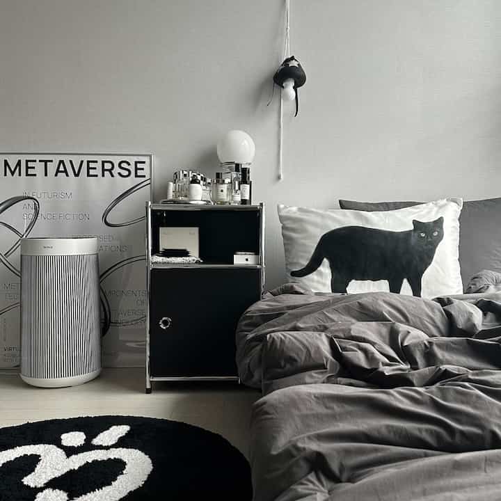A gray and black toned bedroom featuring a black cat pillow and a sleek nightstand within a modern monotone interior