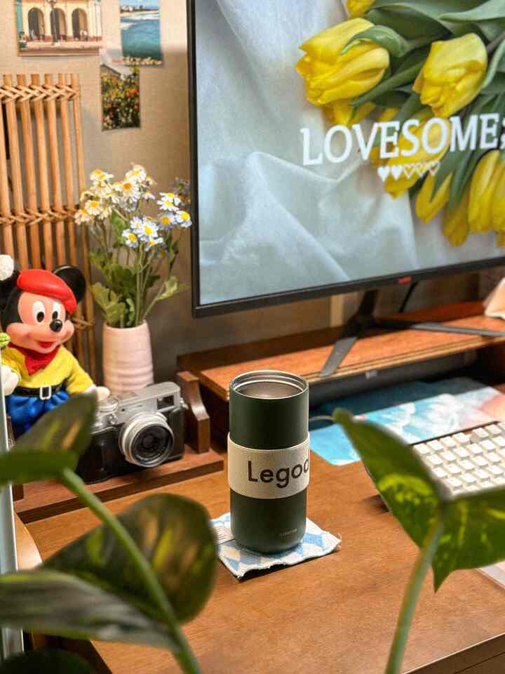 ナチュラルなブラウンの木目調ホームオフィス、中央に木製デスクとタンブラーが配置され、周囲に緑の植物が飾られている