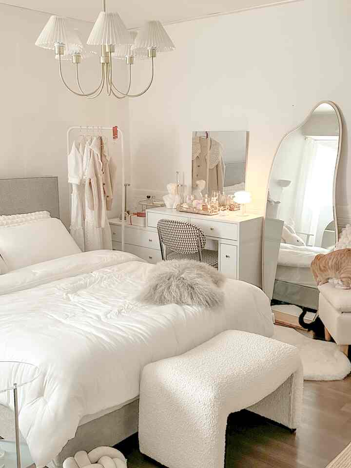 Bright white-toned bedroom featuring a central white bed, vanity with mirror, in a natural modern style setting