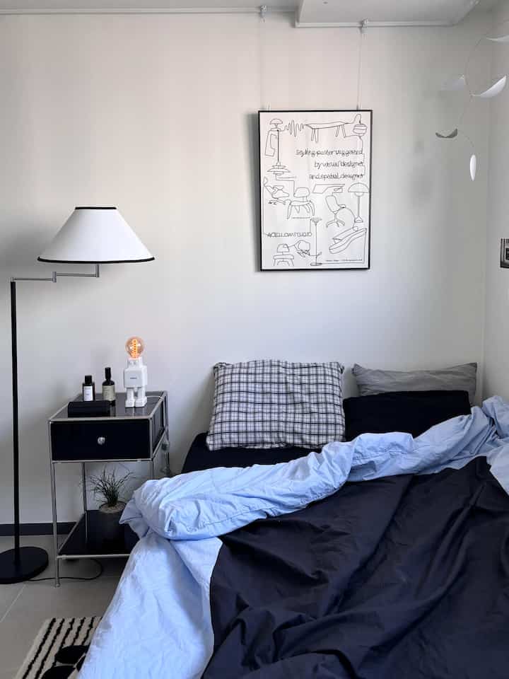 White and gray toned bedroom featuring a tidy bed, floor lamp, and framed wall art, with a simple modern interior