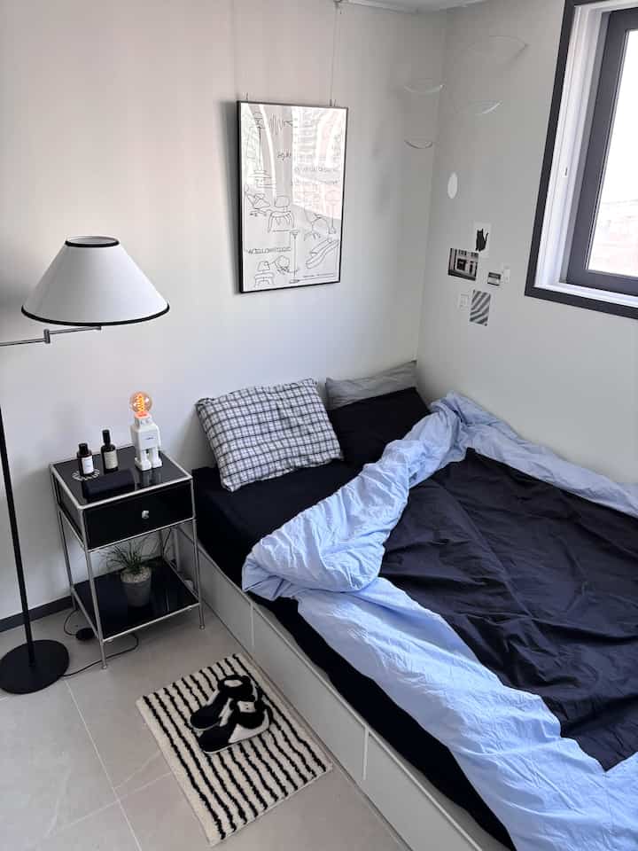 Simple bedroom with white, black, and blue tones featuring bed, nightstand, and mobile creating a sleek atmosphere