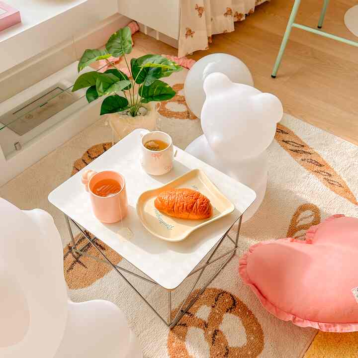 White and brown toned kids' room featuring heart-shaped cushion, bear chair, and coffee table with tea and pastry creating a cozy atmosphere