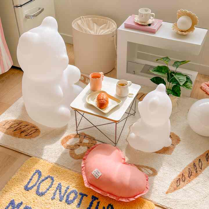 柔らかなナチュラルカラーの寝室、クマ型の照明とハートクッション、かわいらしいおうちカフェアイテムが配置された雰囲気のあるインテリア