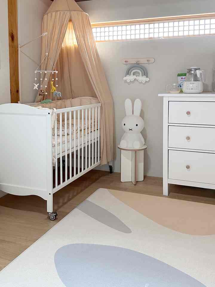 Soft beige and white toned baby room featuring crib, dresser, and cute rabbit lamp creating cozy atmosphere