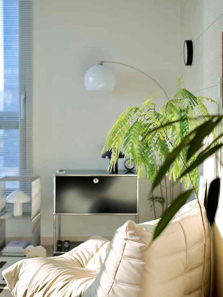 Beige and black toned living room featuring beige sofa, large floor lamp, and green plants in a cozy modern space