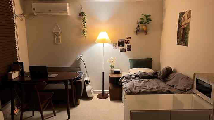 ウォールナットとベージュのトーンのワンルーム、ソファとベッド、グリーンクッションとフロアランプが配置された雰囲気のある空間