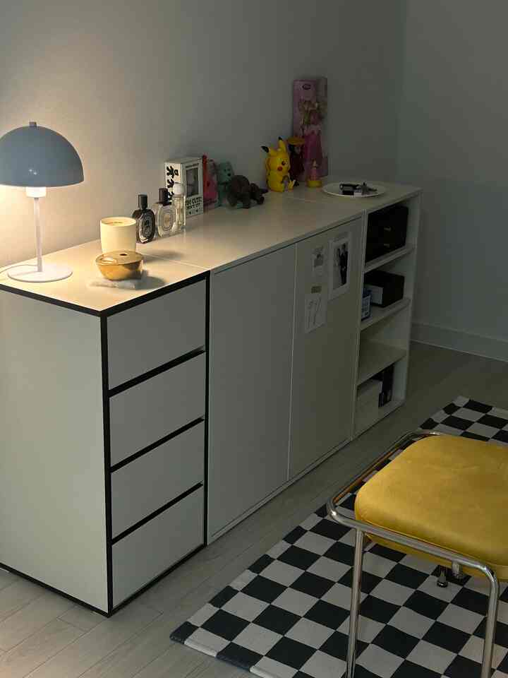 Modern bedroom with white storage cabinet, yellow cushioned stool, and blue table lamp in a clean, minimal setting