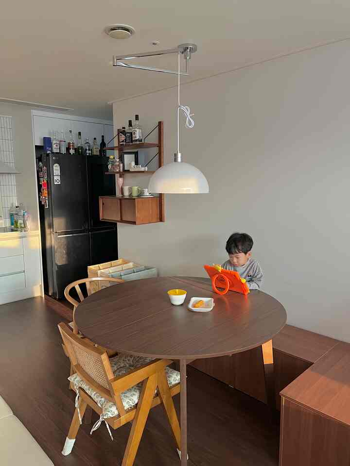 ホワイトと木目調のキッチンに4人用の丸いダイニングテーブルとペンダントライトが配置された温かみのある家族空間