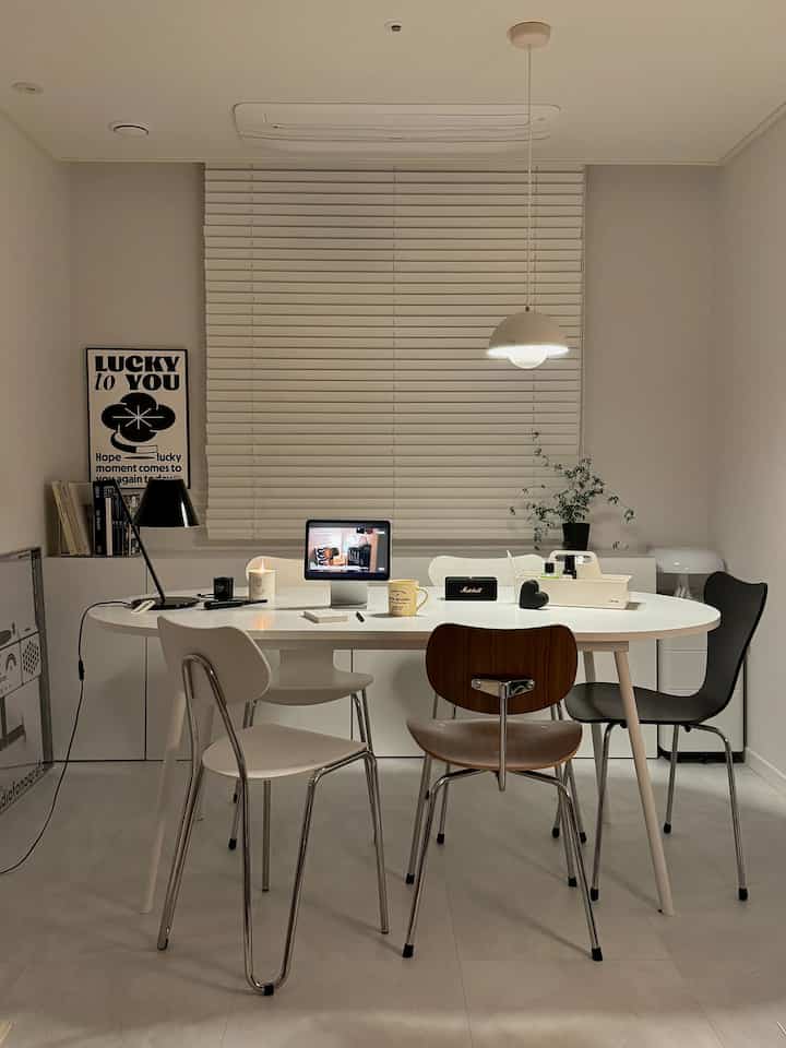 明るい白を基調としたホームオフィス空間、中央に白い楕円形のデスクと多様な色の椅子が配置されたシンプルな雰囲気のインテリア