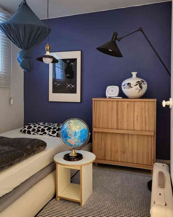 ネイビーの壁と木目調の収納があるコンパクトな寝室、ベッドと壁掛けポスターが印象的な雰囲気を演出