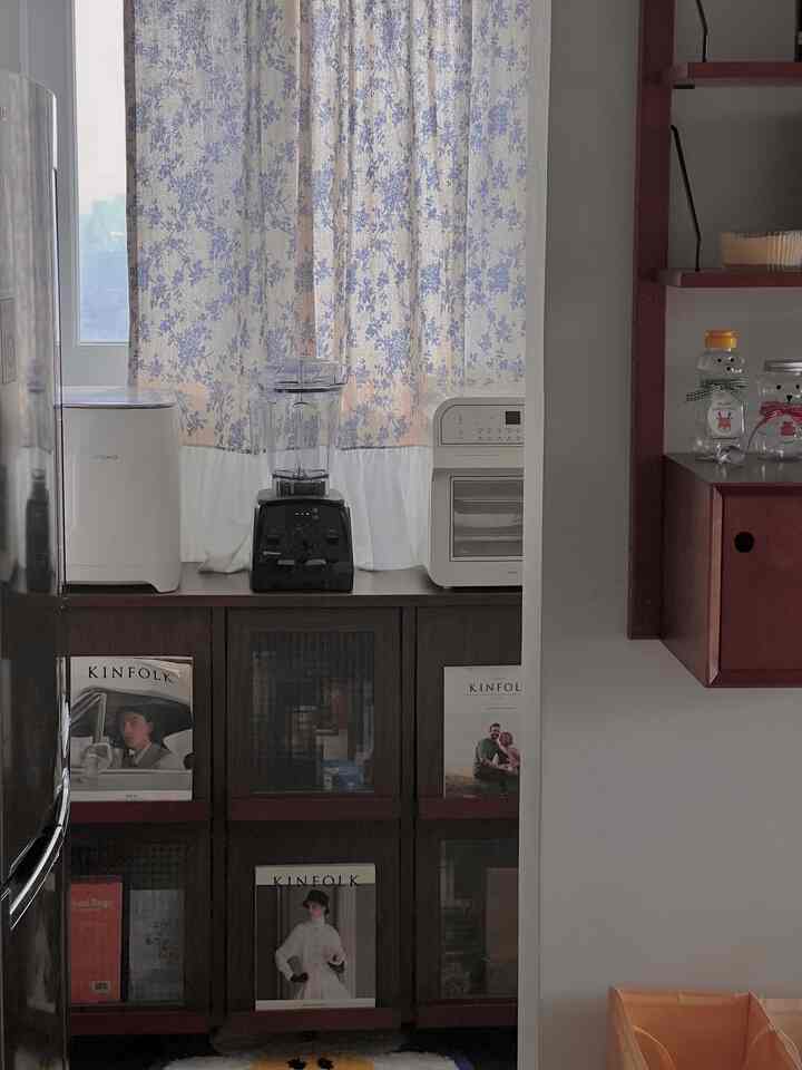 白と茶色の落ち着いた色調のキッチン、窓に花柄カーテンが掛かり、家庭用製氷機とミキサーが置かれたキャビネットが配置された雰囲気のあるインテリア