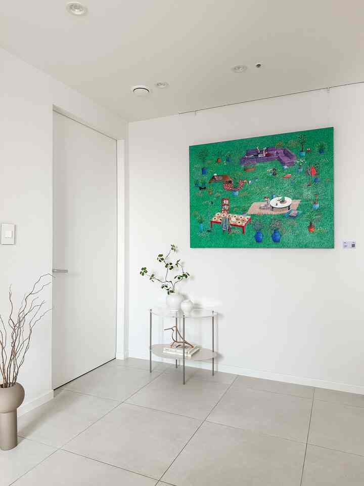 明るいホワイトのリビングまたは玄関空間、シンプルな透明のサイドテーブルと緑の大きな絵画が配置された雰囲気のあるインテリア