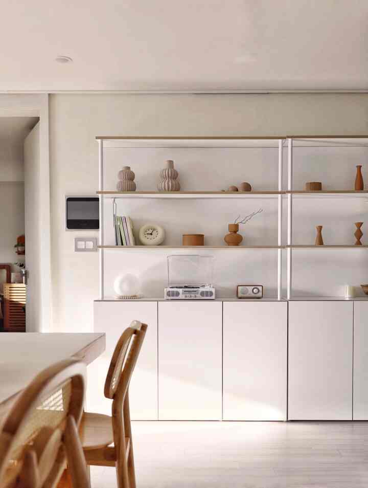 Natural wood tones and white background dining room featuring wooden dining chairs, shelves, and decor in a simple setting