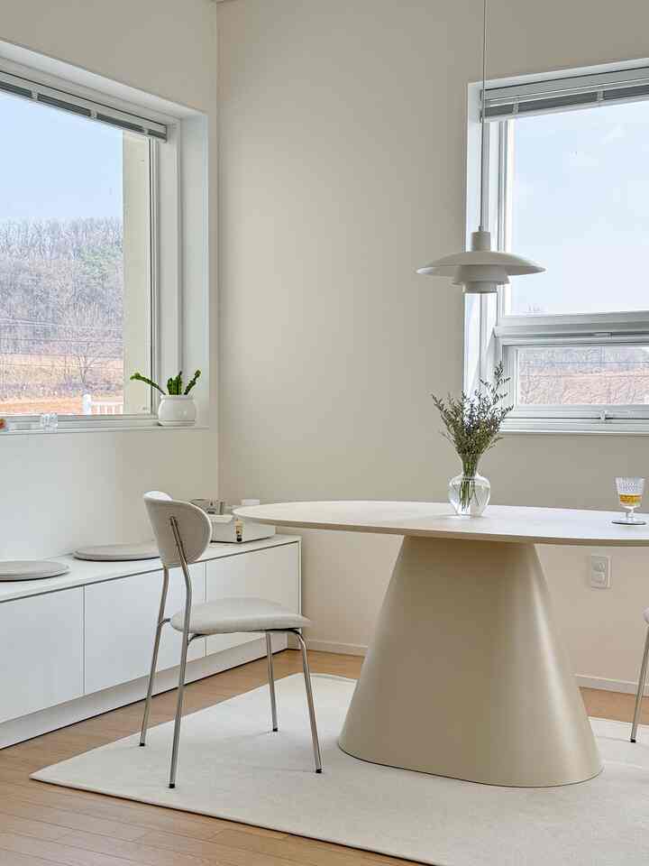 A bright and clean white and natural toned dining room featuring a round ceramic dining table and Volini chairs