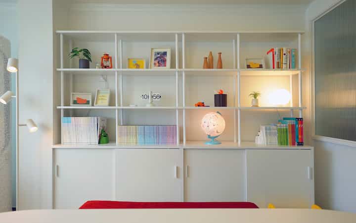 白を基調としたリビングルーム、中央に本棚があり、手前に赤いソファベンチが配された清潔感のある空間
