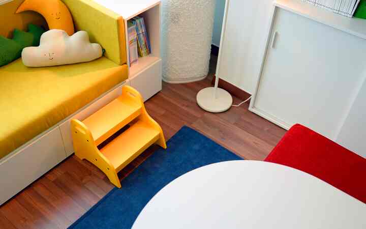 ホワイトトーンの子供部屋、黄色いソファと赤い椅子、青いラグが配置された雰囲気のあるインテリア