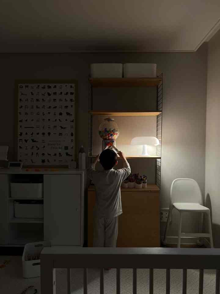 White and natural-toned kids' room featuring child playing near storage shelves with warm, cozy atmosphere