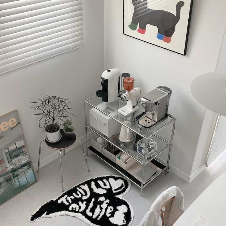 White and black toned dining room with glass shelving holding coffee appliances and cat-themed art in a modern setting