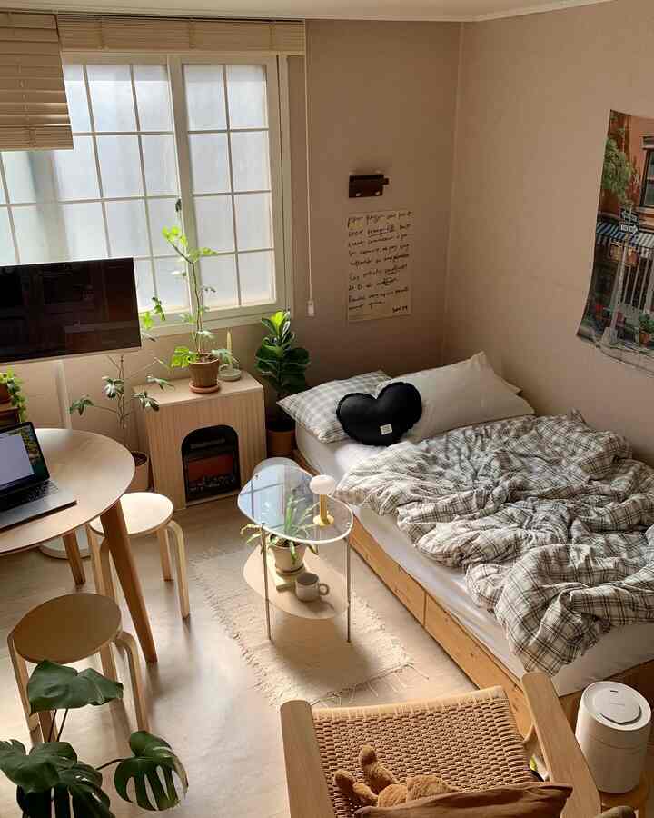 白い壁と木目調の家具が調和した寝室、木製の丸テーブルとチェック柄の掛け布団カバーが温かみのある雰囲気を演出する空間