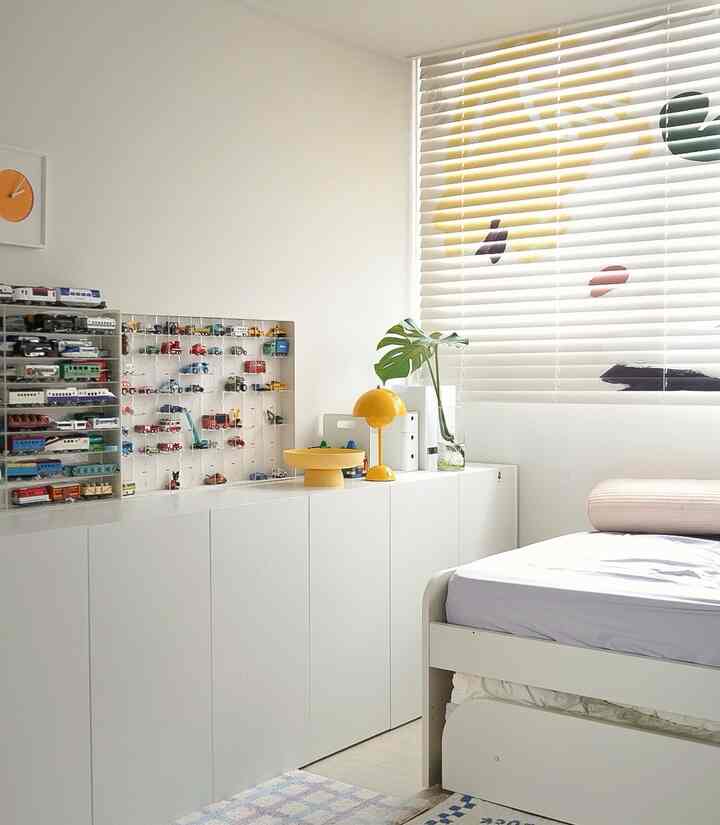 白と黄色のアクセントがある明るい子供部屋、おもちゃの収納キャビネットと快適なベッドが配置された自然な雰囲気の空間