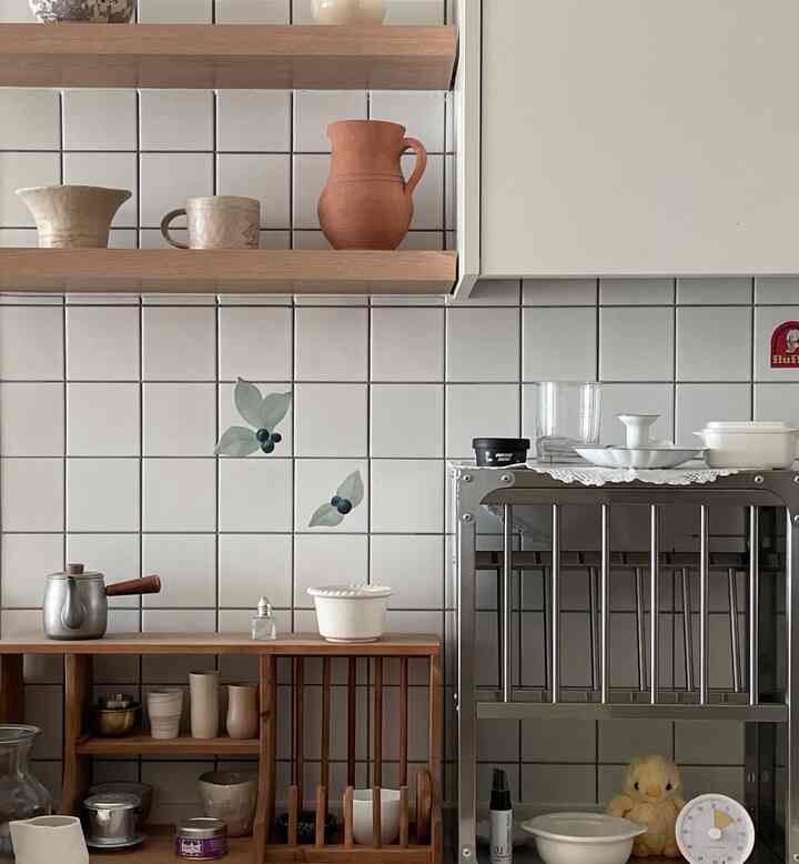 Kitchen space featuring white tiled walls and wood shelves, creating a clean and natural atmosphere