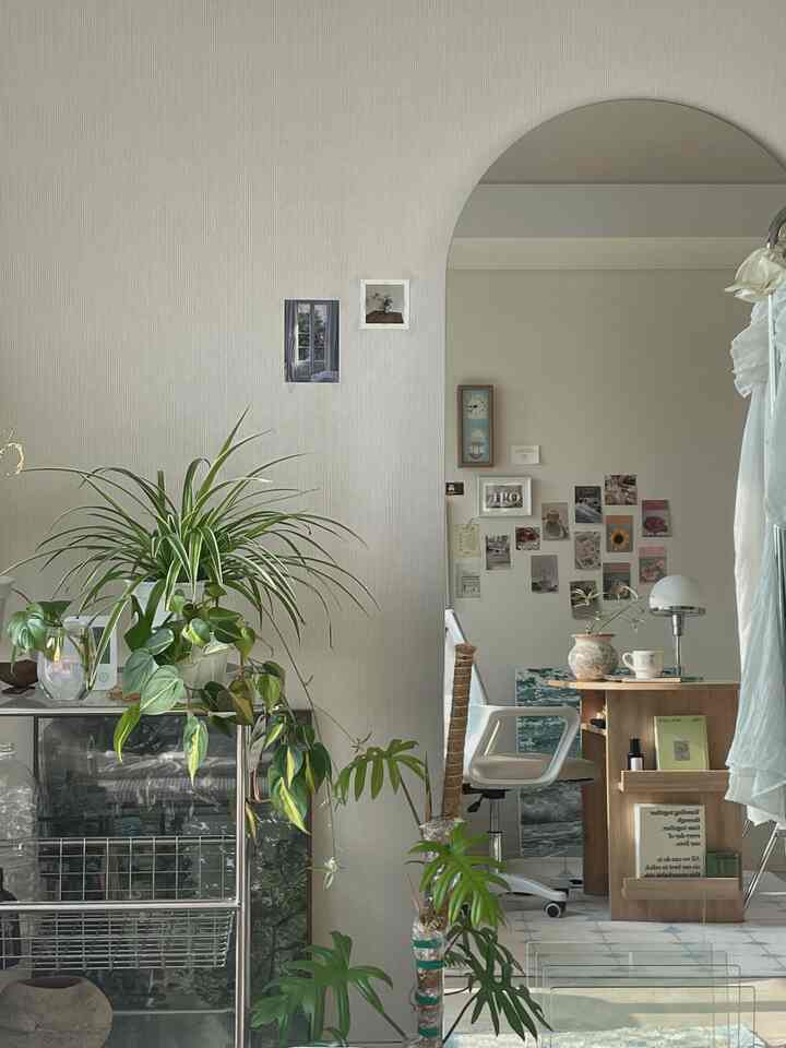 White and green toned studio apartment with plants, desk, and office chair creating a natural and cozy atmosphere