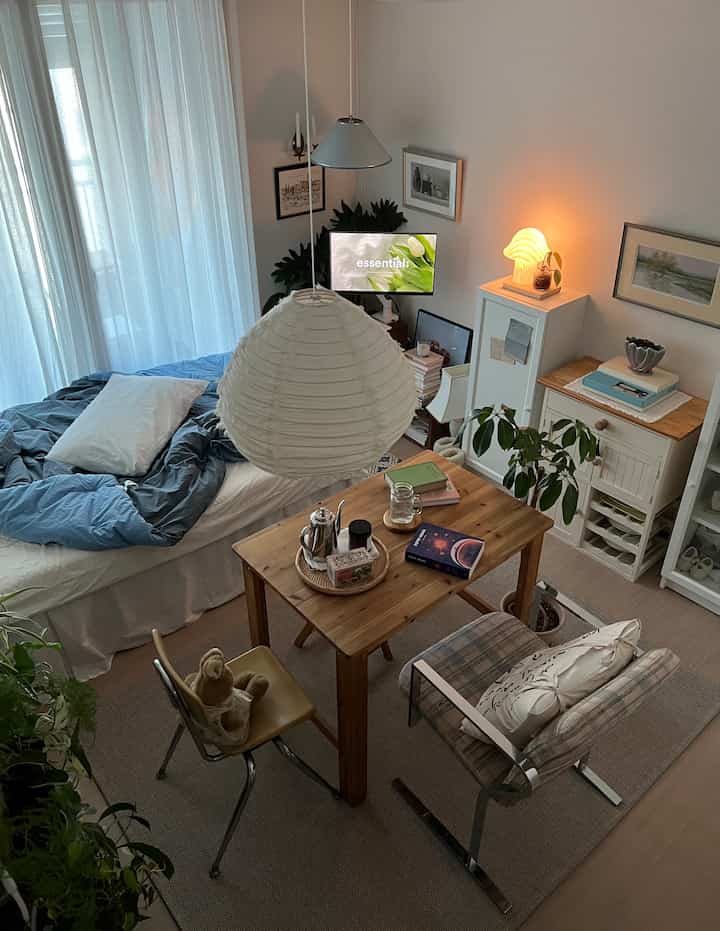 ナチュラルな雰囲気のワンルーム寝室、木製ダイニングテーブルと植物が配置された温かみのある空間