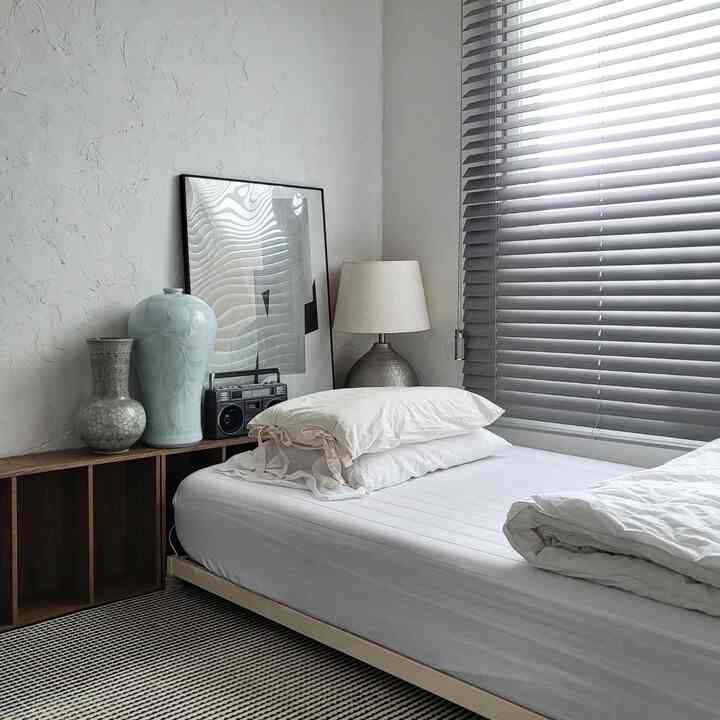 Neutral-tone bedroom featuring wood-tone shelf and white bedding in a minimalistic space