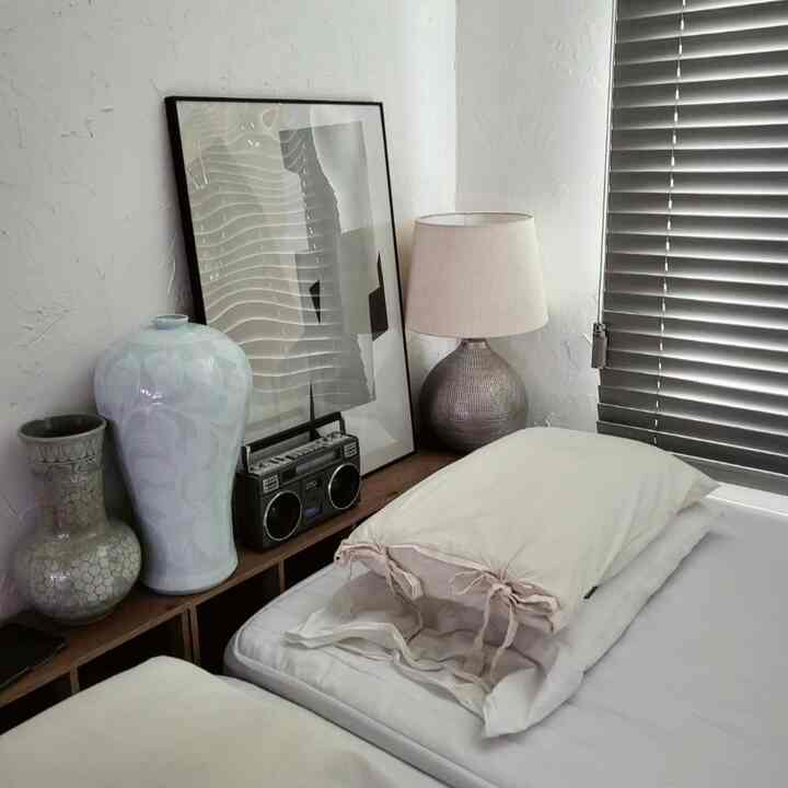 ライトグレーの壁とブラインドがある寝室、木目調の棚とヴィンテージ雑貨が調和するナチュラルモダンなインテリア