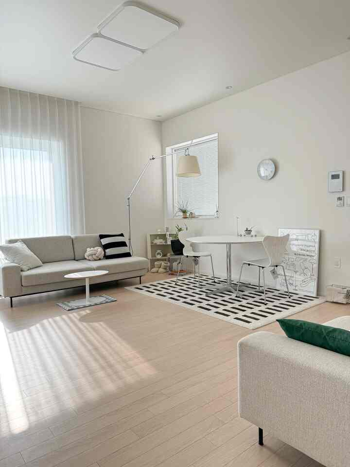 White-toned mid-century modern living room featuring sofas, round dining table and large floor lamp with a clean and bright atmosphere