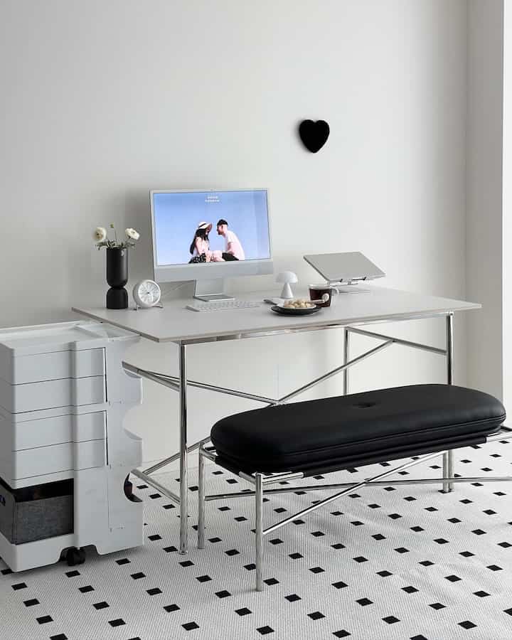White and black toned home office living room with iMac desk, rolling storage unit, and bench seating in a minimalistic space