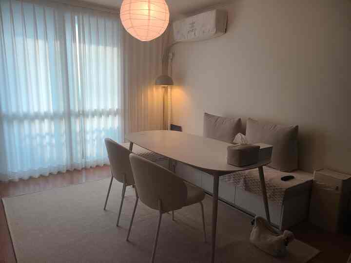 淡いホワイトとナチュラルトーンのコンパクトなダイニング兼リビング空間、楕円形のテーブルとベンチ型ソファが配置された落ち着いたインテリア