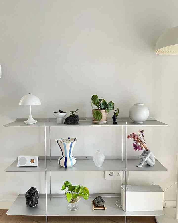White background with metal shelf featuring plants, vases, and objet decor in a minimal natural interior space