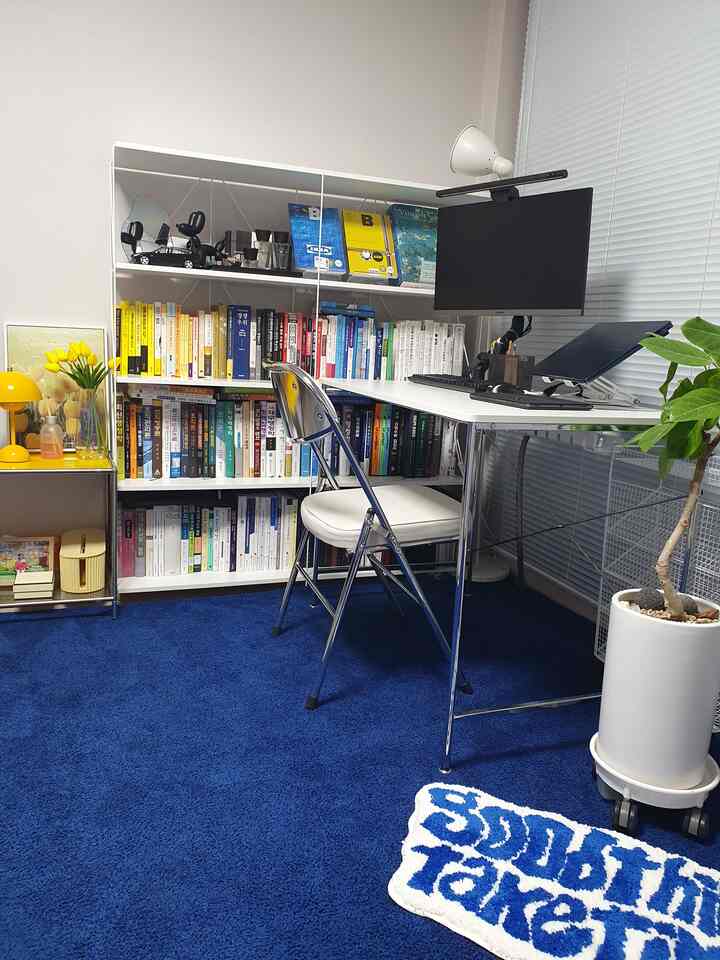 ホワイトとブルーの色調のホームオフィス、書棚とデスク、パソコンモニターが配置された実用的で清潔感のあるインテリア