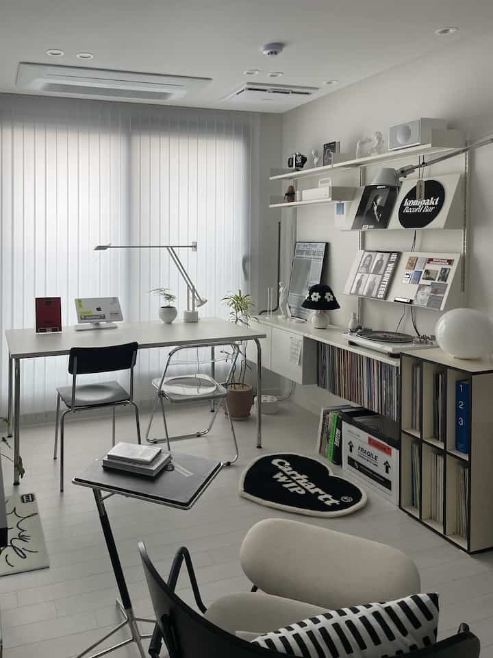 White-toned home office space featuring a simple desk, chairs, bookshelf, and clean layout for organized work