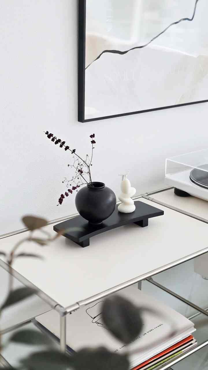 Minimalist living room with white walls featuring a black vase and a white sculpture on a modern light-toned table