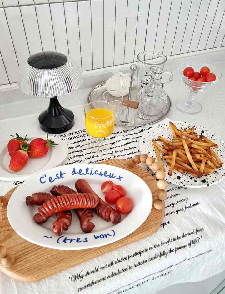 White wall and lighting featuring a wooden cutting board with sausages and tomatoes on a kitchen table in a home cafe style space