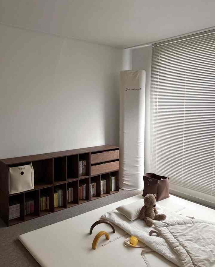 ベージュと木目調の子供部屋、床に置かれた寝具とおもちゃ、整理された収納棚が配置された自然な雰囲気のインテリア